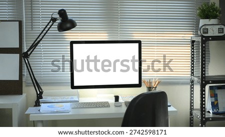 Modern designer workspace with blank computer screen, desk lamp, color charts, and stationery in a creative office.
