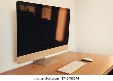 Modern desktop computer with wireless keyboard and mouse on light wooden table. Home office concept. Workplace order. Minimalist interior with white walls