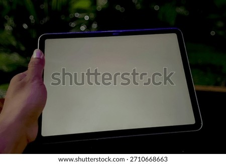 Modern device mockup. High-angle view of a tablet phone resting on a surface, clearly showcasing the blank screen. Blurred vibrant green plants in the background create a fresh, professional context.