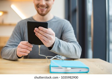 Modern Device. Selective Focus Of An E Reader Being In Hands Of A Smart Positive Young Man While Being Charged