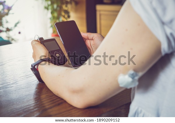 Modern diabetes treatment, woman checking\
glucose level and dosing insulin using insulin pump and remote\
sensor on her hand, focus on\
background