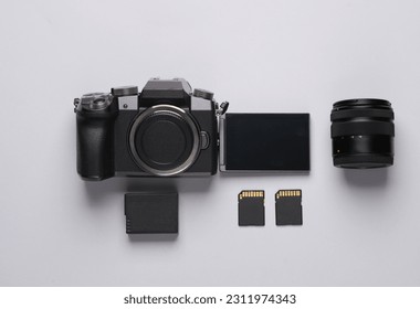 Modern digital camera with flip screen, two sd memory cards, battery and lens on gray background. Photographer's equipment. Top view. Flat lay