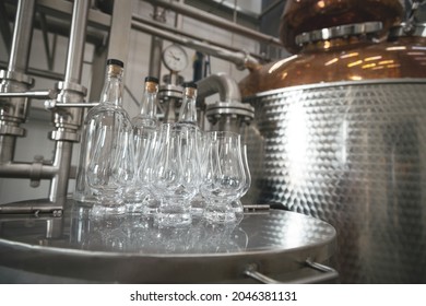 Modern Distillery Equipment. Industrial Equipment For Whisky Production.  Glasses For Whisky Degustation In Front Of Copper Vacuum Still.