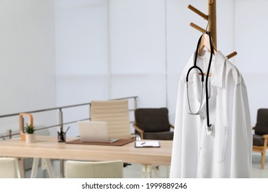 Modern Doctor's Workplace With Wooden Table And White Coat Hanging On Rack In Office