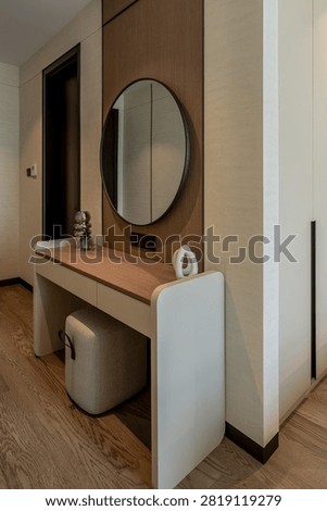 Modern dressing table interior with a round mirror and soft square stool in a luxury home.