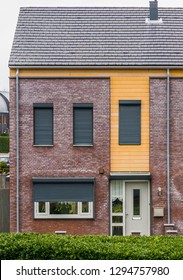 Modern Dutch Terrace House Decorated With Plants Behind The Windows, Some Windows Closed Down With Roller Shutters, Home In A Dutch Small Village