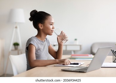 Modern E Education, Social Distance, Study Online With Devices And Health Care At Home, Covid-19. Teen African American Girl Drinking Water At Table With Laptop In Living Room Interior, Profile