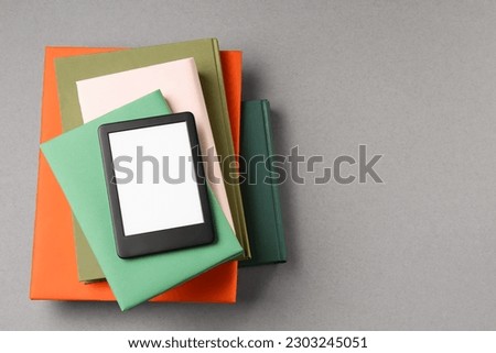 Modern e-book reader and stack of hard cover books on light grey table, top view. Space for text