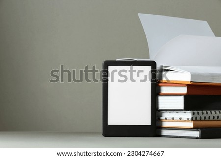 Modern e-book reader and stack of hard cover books on light grey table. Space for text