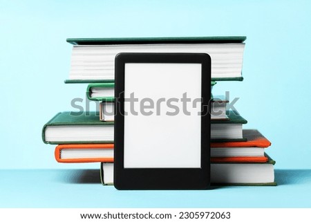 Modern e-book reader and stack of hard cover books on light blue background