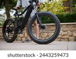 A modern ecologically friendly e-bike in the city, ready for rent. Cropped view of a sporty man riding electric motor bike. Bike sharing city service. Environmental conservation. Sustainable lifestyle