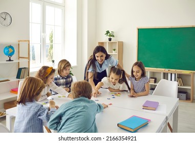 Modern education. Female teacher and junior high school students have fun putting together puzzles in class. Little girls and boys sit in a classroom around the table and play fun games in class. - Powered by Shutterstock