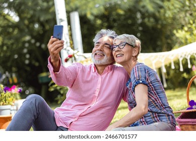 Modern elderly couple taking selfie on smartphone, having picnic and resting in garden at sunny day - Powered by Shutterstock