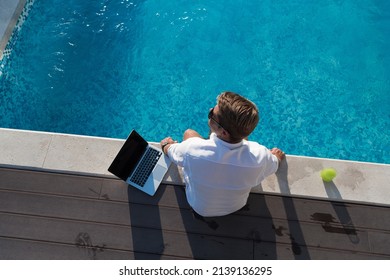 A modern elderly man enjoys the pool while working on his laptop next to a modern luxury house. Selective focus 
