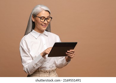 Modern elderly senior woman in formal wear using digital tablet isolated on beige. Portrait of mature female business person using online technology, computer app