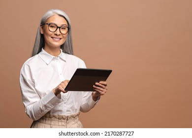 Modern elderly senior woman in formal wear using digital tablet isolated on beige. Portrait of mature female office employee using online technology for doing business, computer app for accounting - Powered by Shutterstock