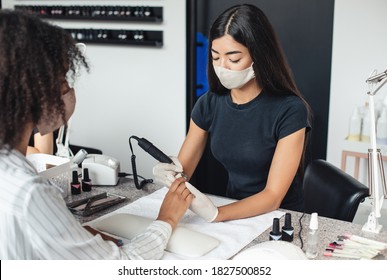 Modern Electric Device And Reopening Of Beauty Salon After Quarantine. Asian Master In Protective Mask And Gloves Doing Hardware Manicure For African American Woman In Studio With Nail Equipment