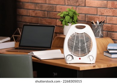 Modern electric fan heater near laptop and notebooks on wooden table in office