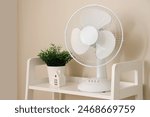 Modern electric fan with houseplant on shelving unit at home