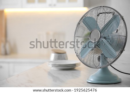 Modern electric fan on countertop in kitchen, space for text. Summer heat