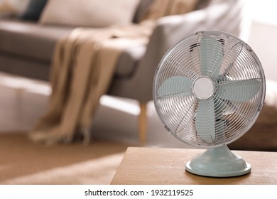 Modern electric fan on wooden table in living room. Space for text