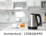 Modern electric kettle, cup and honey on wooden table in kitchen