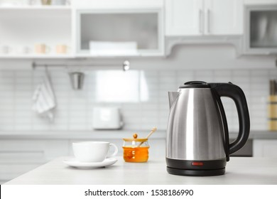 Modern electric kettle, cup and honey on wooden table in kitchen