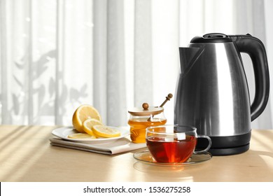 Modern Electric Kettle And Cup Of Tea On Wooden Table Indoors. Space For Text