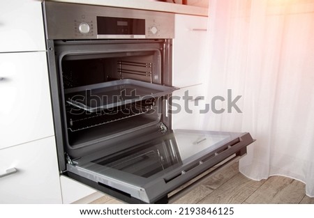Modern electric oven with telescopic rails and steel baking tray. Hinged oven door. Black oven in a white kitchen. Automatic cooking program
