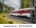 Modern electric passenger train enters the train station. Summer landscape in background. Red passenger wagons.