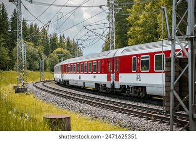 Modern electric passenger train enters the train station. Summer landscape in background. Red passenger wagons. - Powered by Shutterstock