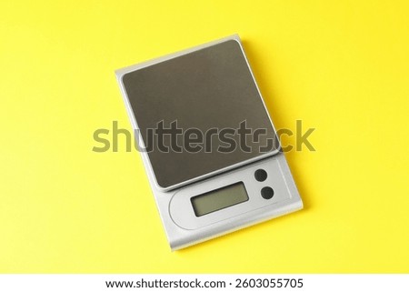 Modern electronic kitchen scale on yellow background, above view