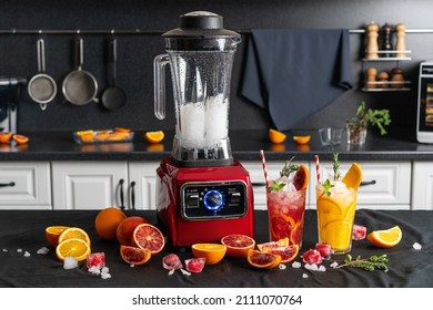 Modern electronic Red blender with crushed ice cubes and cold homemade citrus lemonade in faceted glasses with cardboard cocktail tubes. home kitchen background.