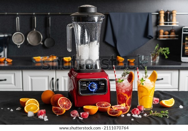 Modern electronic Red blender\
with crushed ice cubes and cold homemade citrus lemonade in faceted\
glasses with cardboard cocktail tubes. home kitchen\
background.