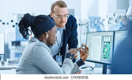 Modern Electronics Factory: Female Supervisor Talks To A Male Electrical Engineer Who Works On Computer With CAD Software. Designing PCB, Microchips, Semiconductors And Telecommunications Equipment