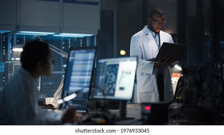 Modern Electronics Research, Development Facility: Professional Black Engineer Holding Laptop Computer Standing In The High-Tech Laboratory. Scientists Design Silicon Microchips, Semiconductors