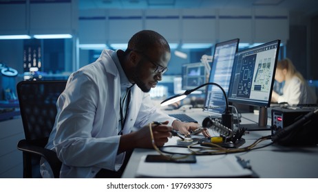 Modern Electronics Research, Development Facility: Black Male Engineer Does Computer Motherboard Soldering. Scientists Design PCB, Silicon Microchips, Semiconductors. Medium Closeup Shot