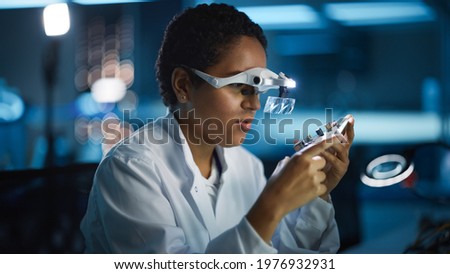 Modern Electronics Research and Development Facility: Beautiful Black Female Engineer Inspects Printed Circuit Board Motherboard. Scientist Designs Industrial PCB, Silicon Microchips, Semiconductors