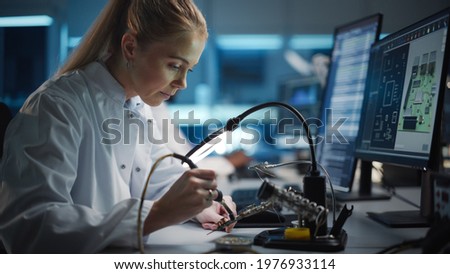Modern Electronics Research and Development Facility: Beautiful Caucasian Female Engineer Does Computer Motherboard Soldering. Scientists Design Industrial PCB, Silicon Microchips, Semiconductors