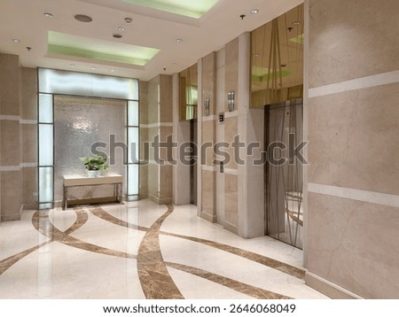 A modern and elegant elevator lobby in a luxury hotel or office building. The space features polished marble floors with a distinctive pattern, soft ambient lighting, and clean architectural lines. 