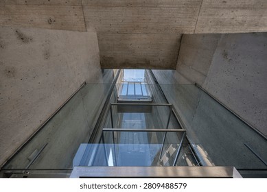A modern elevator shaft featuring transparent glass walls framed with metal and surrounded by textured concrete surfaces in a contemporary architectural setting.