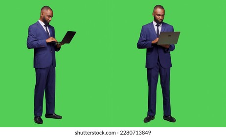 Modern employee using laptop to browse network, looking at online website standing over full body greenscreen. Young adult businessman working with wireless computer in studio. - Powered by Shutterstock