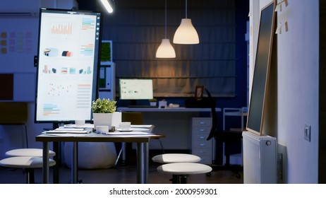 Modern Empty Business Corporate Office Meeting Room Ready For Businesspeople Late At Night. In Background On Conference Table Standing Company Financial Documents With Economy Graphs