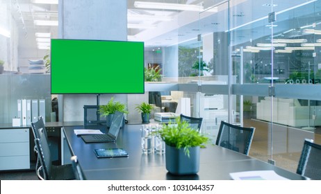 Modern Empty Meeting Room With Big Conference Table With Various Documents And Laptops On It, On The Wall Big TV With Green Chroma Key Screen.