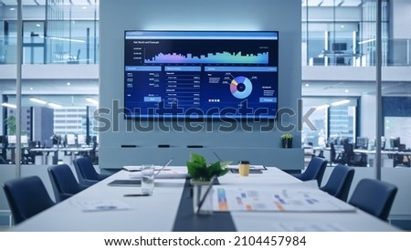 Modern Empty Meeting Room with Big Conference Table with Various Documents and Laptops on it, on the Wall Big TV with Big Data, Statistics, Talks about Company Growth. Contemporary Designed Workplace.