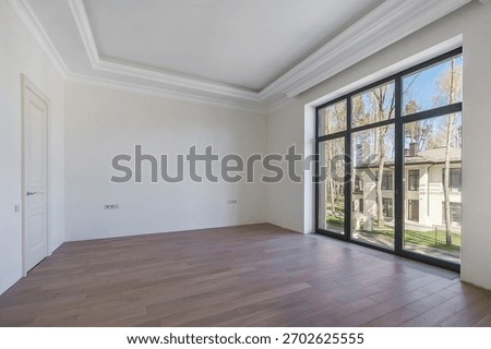 A modern, empty room with large windows that overlook a quiet garden in a prestigious area in bright daylight.