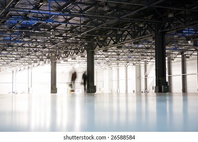 Modern Empty Storehouse With Lights At Far Side And Silhouettes Of Two People Walking Away