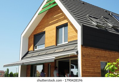 Modern energy efficient wooden house with skylights and solar panel on asphalt shingled roof, windows with roller shutters and outdoor canopy retractable roof, patio awning. 