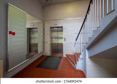 Modern entrance interior in living complex. Big mirror, elevator and stairs. Rug on red tile.