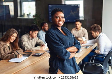 Modern entrepreneur concept. African american businesswoman standing with folded arms in conference room during meeting with colleagues and smiling at camera - Powered by Shutterstock